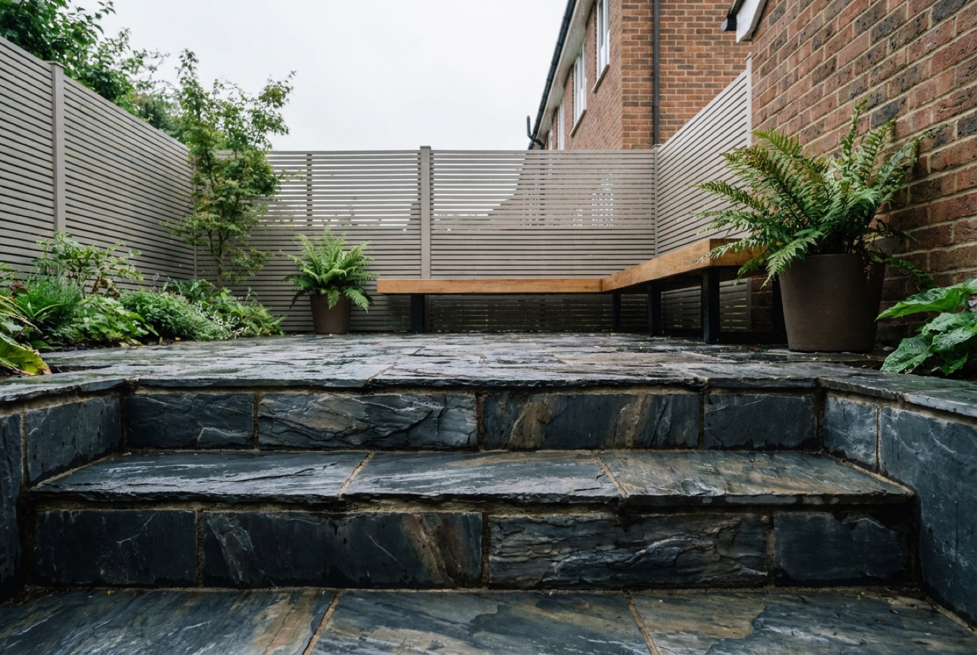 Dark riven slate steps and paving in a contemporary UK garden, wet from rain and rich in colour